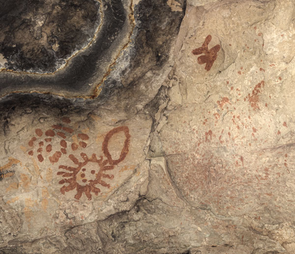 Dots, sun, open oval, and other figures painted in red on a natural stone wall, Walnut Canyon site WACA 180